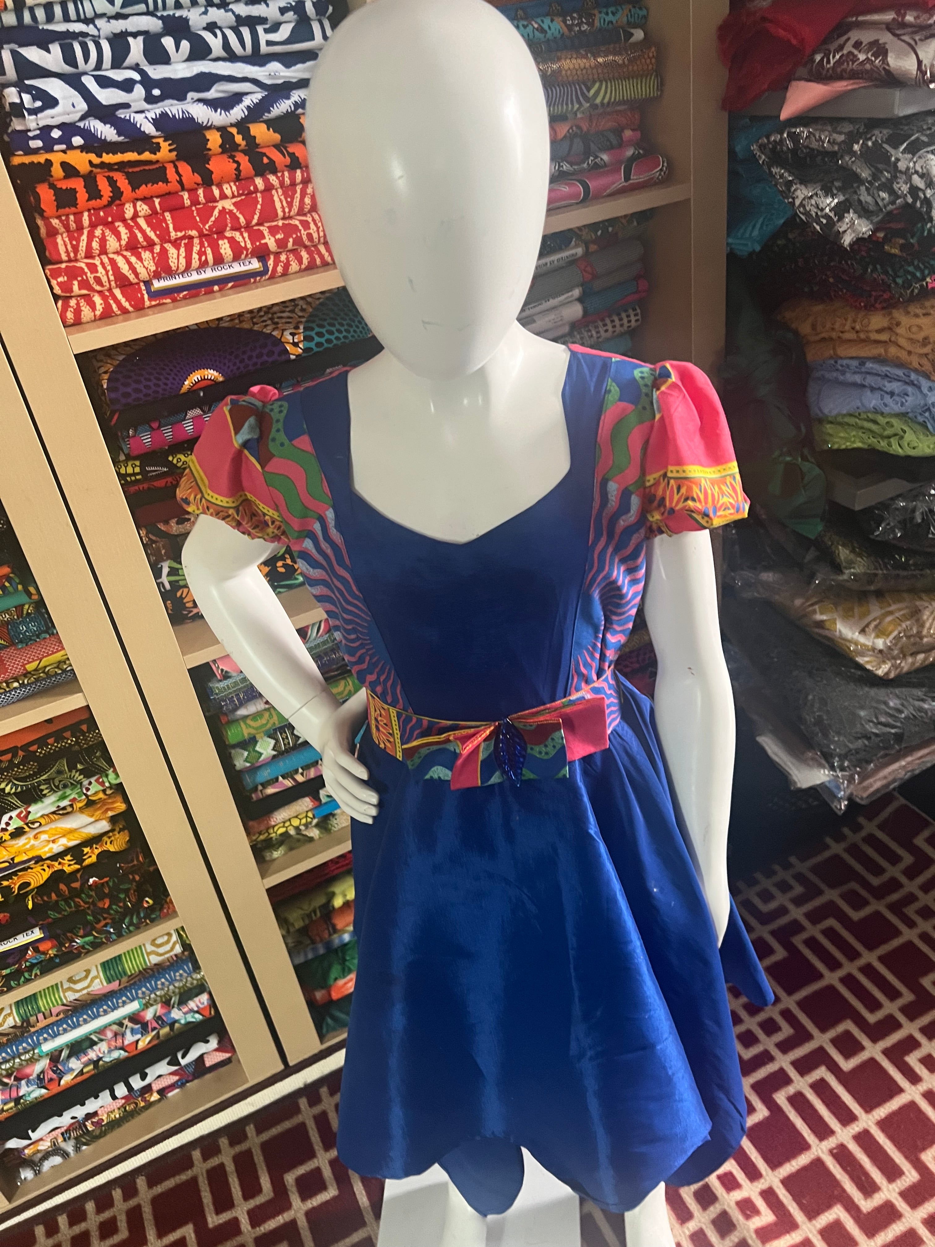 A children's dress designed for ages 7 to 10, featuring coordinating taffeta and Ankara fabric, finished with a stylish knot et the back